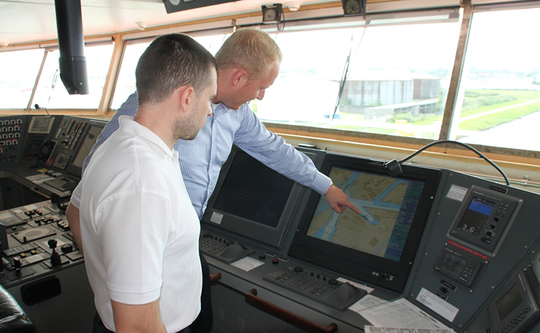 Eine Person erklärt einer anderen Perosn in der Kommandobrücke die Route auf einem Monitor Eine Person erklärt einer anderen Perosn in der Kommandobrücke die Route auf einem Monitor
